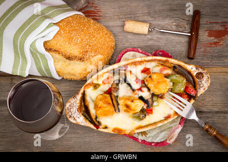 Huhn und Gemüse Eintopf mit einem frischen knusprigen Laib von Sesam-Brot und ein Glas Rotwein auf einem alten verwitterten Holztisch mit Stockfoto