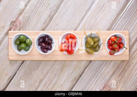 Blick von oben auf eine Reihe von sortierten geheilt herzhaften Oliven und Paprika in einzelnen Schnupper-Platten auf einem Holzbrett auf einem Holz ta Stockfoto