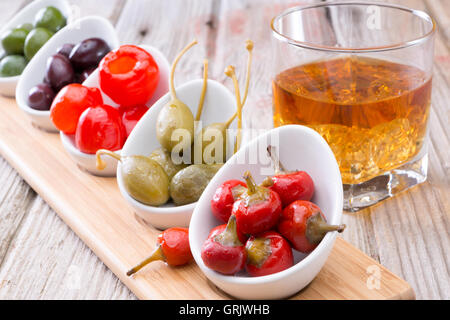 Herzhafte kleine rote Piment, Paprika und Oliven serviert mit einem Tumbler Whiskey auf einem alten rustikalen Theke Stockfoto