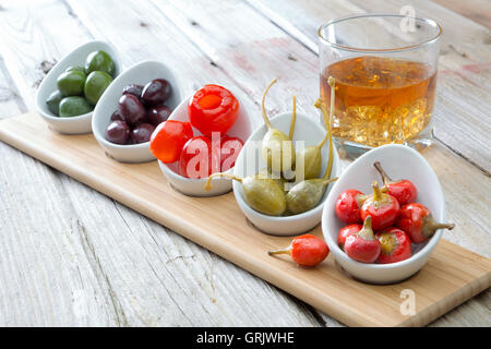 Auswahl an herzhaften schwarze und grüne Oliven und rote Piment Paprika in Schälchen für Snacks serviert mit einem Glas Whiskey auf Stockfoto