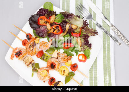 Portion leckere pikante Garnelen Spieße mit Paprika und Tomaten serviert mit einem Salat von frischem Blattgemüse, Overhead o anzeigen Stockfoto