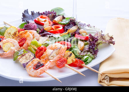 Garnelen-Spieße mit Paprika und Tomaten serviert mit einem frischen gemischten Salat für ein Abendessen mit köstlichen Meeresfrüchten, niedrigen Winkel hautnah Stockfoto