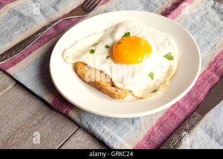 Gebratenes Ei auf Brot zum Frühstück auf Teller und rustikalen Tisch Stockfoto