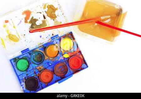 Top-down-Ansicht verwendet der alten Aquarell Palette mit Pinsel in Tasse mit Wasser auf weißem Papier. Stockfoto