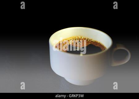 Kaffeetasse auf einem Glastisch. Weiße Kaffeetasse hautnah mit dunklem Hintergrund und dramatisches Licht. Stockfoto
