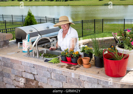 Ältere Dame arbeitet in ihrem Sommerküche auf einem gemauerten Terrasse Pflege und Topfen Sie ihre Zimmerpflanzen in einer Vielzahl Stockfoto