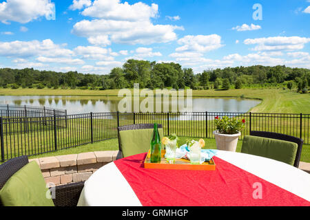 Gläser mit frischem Eiswasser, garniert mit frischer Minze und Zitrone auf einem Gartentisch abgedeckt in einem bunten roten Tuch mit Blick auf eine Stockfoto