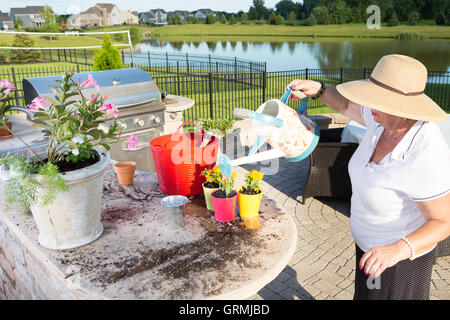 Ältere Dame in einem breitkrempigen Sonnenhut steht auf einer Terrasse im freien Gießen ihr neu Topfpflanzen in der Sommerküche mit einem Stockfoto