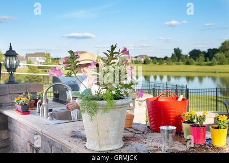 Ältere Dame, die ihre Blüte dekorative Zimmerpflanzen steht an der Spüle in ihre Sommerküche auf einer Terrasse im freien Wate tendenziell Stockfoto