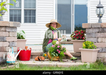 Großmutter Blumenerde Pflanzen auf ihrer Terrasse sitzen auf dem Backstein-Schritt umgeben von frischen Setzlinge und Blumentöpfe auf der Suche pensiv Stockfoto