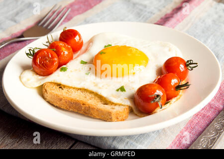Gebratenes Ei auf Brot und Tomaten zum Frühstück auf Teller und rustikalen Tisch