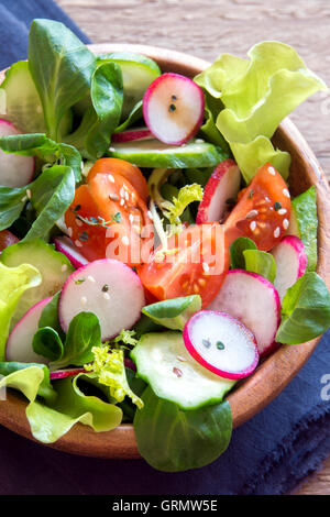 Frisches Grün Frühling Gemüsesalat mit Gurke, Radieschen, Tomaten und Samen in Holzschale hautnah Stockfoto