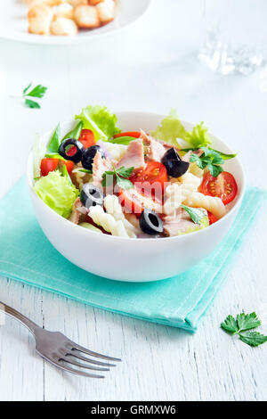 Thunfisch und Pasta-Salat mit frischen Tomaten, Oliven, Kräuter in Schüssel über weißem Holz Hintergrund Stockfoto