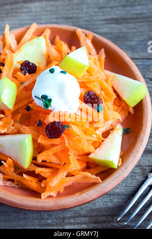 Karotte und Apfel-Salat mit Rosinen, Joghurt und Kräuter in rustikalen Keramikschale hautnah Stockfoto