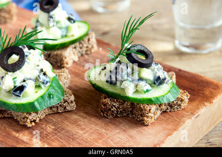 Mini-Sandwiches (Snacks) mit Gurken, Oliven und Fisch Salat über rustikale Holz Hintergrund Stockfoto