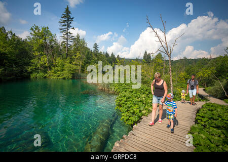 Urlauber, die ein Spaziergang auf einem hölzernen Ponton, gesäumt von Pestwurze entlang des Flusses Korana (Nationalpark Plitvicer Seen - Kroatien). Stockfoto