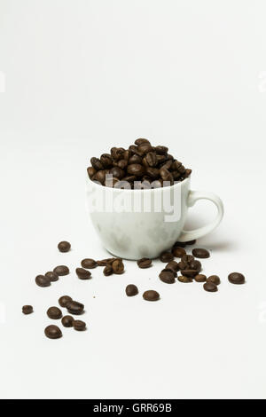 Kaffee-Tasse mit Kaffeebohnen gefüllt und nach dem Zufallsprinzip verteilt Bohnen im Vordergrund. Stockfoto