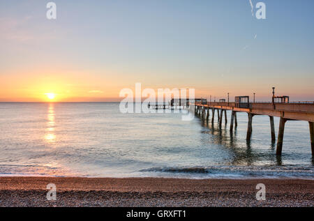 Sunrise, Sunup in klaren, blauen Himmel mit orange Band auf clam Meer über die konkreten Pier an der Kent Küstenstadt beschäftigen. Kiesstrand im Vordergrund. Stockfoto