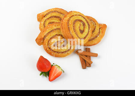 süße Zimtbrötchen, Zimtstangen und Erdbeeren auf weißem Hintergrund Stockfoto