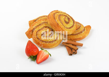 süße Zimtbrötchen, Zimtstangen und Erdbeeren auf weißem Hintergrund Stockfoto