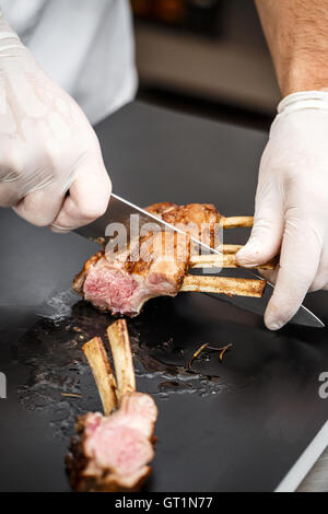 Koch in Scheiben geschnitten Lammrücken in aromatischen Olivenöl, Kräutern und Gewürzen gebraten Stockfoto