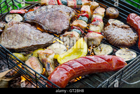 Verschiedene leckere Fleisch mit Gemüse kochen am Grill mit Flammen. Stockfoto