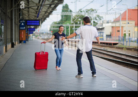 Fliehen Sie bei einer leeren Plattform, eine junge Frau mit einem roten Koffer. Freudige Lächeln auf ihrem Gesicht. Der junge Mann trifft sie. Er ist bereit, hu Stockfoto