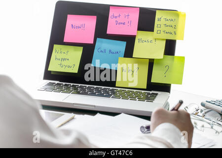 Geschäftsmann auf seinem Schreibtisch mit Haftnotizen mit Nachrichten, einem Laptop-Computer-Bildschirm arbeiten. Das Konzept der anstehenden Arbeit. Stockfoto