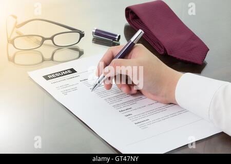 Geschäftsmann oder Arbeitsuchende überprüfen seinen Lebenslauf auf seinem Schreibtisch vor dem Senden an einen neuen Arbeitsplatz mit Stift, Krawatte, Gläser und digital Stockfoto