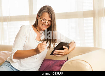 mittlere gealterte Frau mit Brille, lächelnd und Notizen Stockfoto