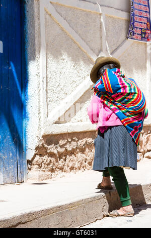 Maras Peru-Mai 18: einheimische Quechua-Frau mit schönen Farben, die zu Fuß in Richtung einer blauen Tür. 18. Mai 2016, Maras Peru. Stockfoto