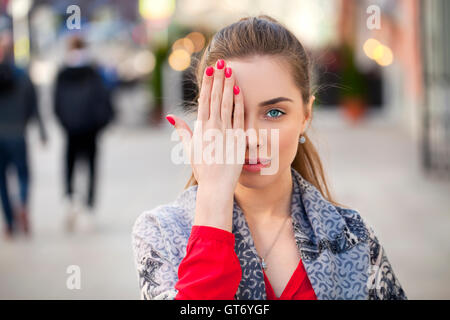 Junge schöne Frau schließt die Augen mit der Hand auf einem Hintergrund von der Straße Stockfoto