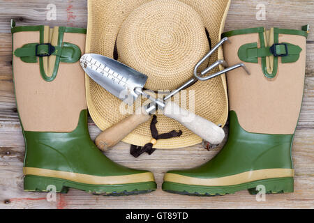 Zubehör für einen modischen Gärtner mit stilvollen Kautschuk Gummistiefel, ein Stroh Hut mit breiter Krempe und gekreuzten Gartenarbeit Utensilien oder Stockfoto