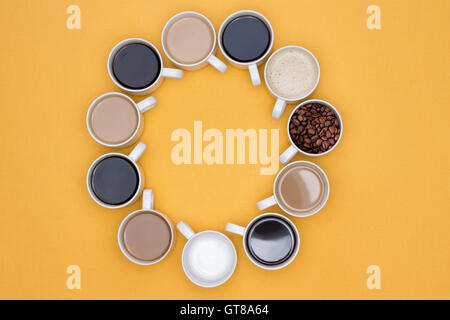 Tassen heißen Kaffee in verschiedenen Geschmacksrichtungen in Kreis auf einem gelben Hintergrund angeordnet in High Angle View erfasst. Stockfoto