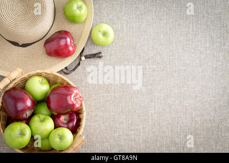 Bauernhof frische rote und grüne Äpfel direkt vom Bauern in einem Korb und auf eine breite Krempe Stroh Sonnenhut auf eine at von oben gesehen Stockfoto