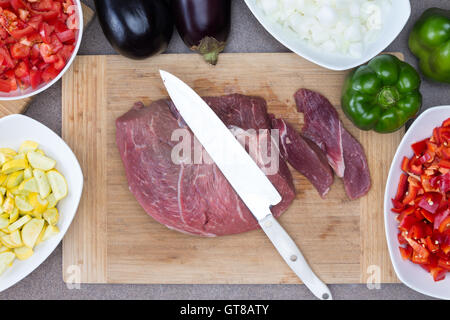 Nahaufnahme frisches Schweinefleisch oder Rindfleisch auf einem Hacken Holzbrett mit Messer umgeben von anderen Zutaten auf Seiten für Kochen Prep Stockfoto