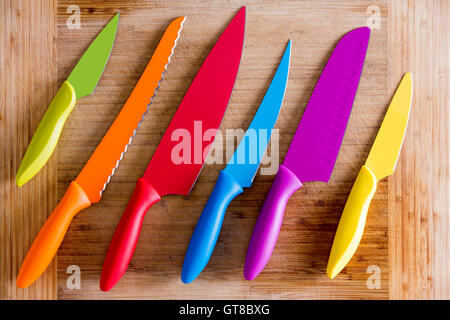 Bunte Küchenmesser mit unterschiedlichen Zwecken auf einem Holzbrett schneiden, Captured in High Angle View hautnah. Stockfoto