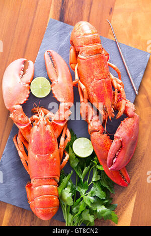 Nahaufnahme, appetitlich bereit zu Essen gekocht Hummer Duo auf ein Schneidebrett mit Kalk und Petersilie, serviert auf einem Holztisch. Stockfoto