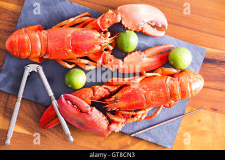 Nahaufnahme gekocht rot Hummer Duo auf ein Schneidebrett grau mit Kalk und Cracking Tool auf einem Holztisch. Stockfoto