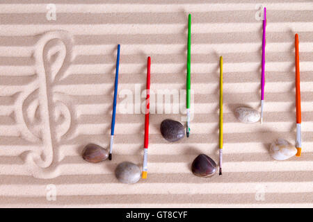 Musik am Meer-Konzept mit einer künstlerischen Anordnung der Noten gebildet aus Kieselsteinen und bunten Pinsel auf dem Rücken Stockfoto