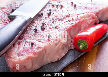 Mariniertes Steak Fleisch mit ganzen schwarzen Pfeffer auf ein Schneidebrett mit rotem Pfeffer und Messer hautnah Stockfoto