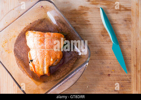 Frisch gebackener Lachs frisch aus dem Ofen in eine Glasschale Ofen neben einem blauen scharfen Küchenmesser auf eine Holzküche Inter Stockfoto