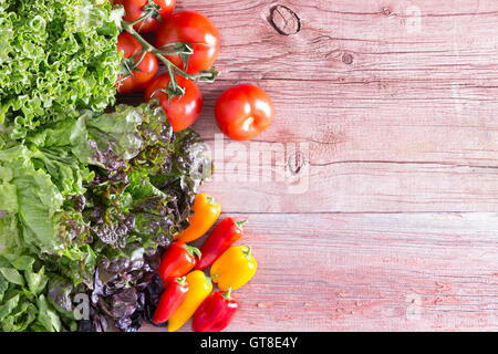 Draufsicht auf urigen Holzbrettern mit abblätternde Farbe von drei verschiedenen Salatsorten mit frischen Tomaten und roten bzw. Stockfoto
