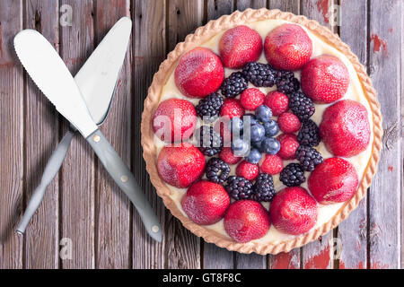 Frische Beeren hausgemachte Torte mit Utensilien, serviert auf einem rustikalen Holztisch gelegt. Über Ansicht. Stockfoto