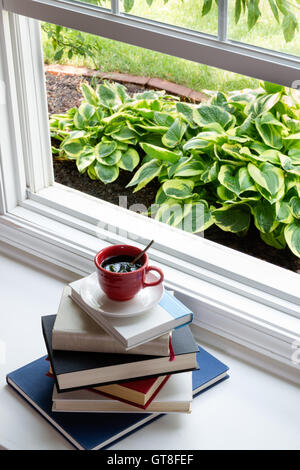 Tasse heißen Kaffee auf gestapelten Bücher neben offenen Glas-Fenster für das Konzept lesen. Stockfoto