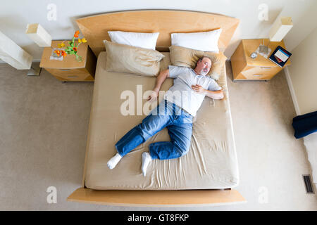 Draufsicht auf ein großes Übergewicht Mann mittleren Alters mit einem Spitzbart liegen ausgestreckt diagonal in Socken auf einen König unter-Size-Bett Stockfoto