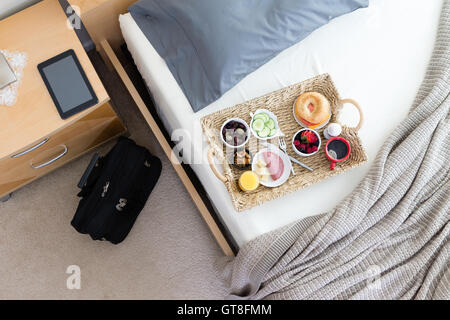 High Angle View of Frühstückstablett auf ungemachten Bett im Hotelzimmer in Business Trip Konzept Bild mit schwarzen Aktenkoffer Tasche und Comput Stockfoto