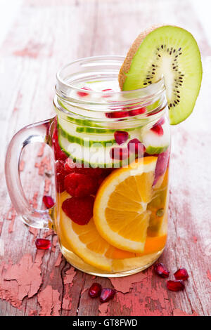 Frisches Obst und Wasser gefüllt Einmachglas mit in Scheiben geschnittenen Orangen, Gurken, Himbeeren, Granatapfel und Kiwis für eine köstliche ref Stockfoto