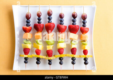 Gesunde bunte frische Schaschlik Obst Leckereien aus saisonalen Sommer tropische Früchte fein säuberlich in einer Reihe auf einem modernen wh angeordnet Stockfoto