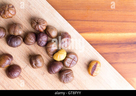 Lecker frisch gerösteten ganze Kastanien verstreut auf einem diagonalen Holzbrett auf einem Holztisch mit Textfreiraum, Ansicht von oben Stockfoto